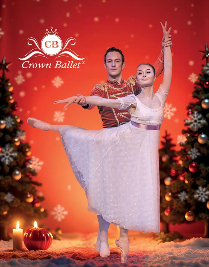Ein Balletttänzer in rotem Kostüm hält eine Tänzerin in weißem Kleid in Pose, umgeben von weihnachtlich geschmückten Tannenbäumen und Kerzen, vor rotem Hintergrund mit Schneeflocken.