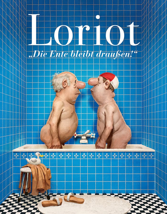 Man sieht ein Blau gekacheltes Badezimmer, in der Mitte hinter dem schwarz weißen Schachbrett Boden ist die Badewanne in der sich zwei gezeichnete Männer Nackt gegenüber stehen und anschauen, der rechte Mann trägt eine weiß rote Badehaube. Vor der Wanne steht ein Hocker auf dem eine Braune Jacke liegt und darauf eine Badeente. Auf dem Teppich vor der Wanne liegen zwei Hausschuhe.